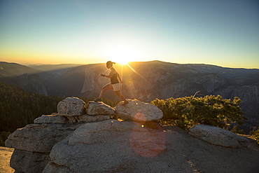 A hiker walks along rocks at Sentinel Dome in Yosemite National Park at sunset.