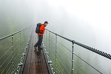 A man looks over a suspension bridge on a rainy fall day in Squamish, British Columbia.