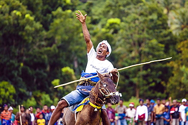 Man raising hand and riding horse with spear at Pasola Festival, Sumba island, Indonesia