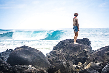 A woman stands on the rocks to look at the waves near Tunnels Beach, Kauai, Hawaii