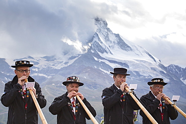 Four traditionally dressed locals playing alphorn against Matterhorn mountain, Zermatt, Valais, Switzerland