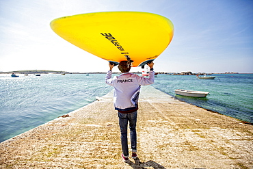 Pierre Le Coq carries his windsurfing board over his head on a jetty at Plouguerneau, Brittany, France.