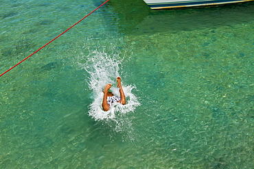 Boy jumps into water from wooden pier on West End, Roatan, Honduras