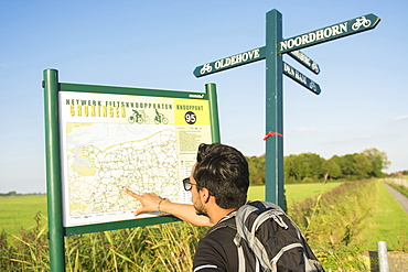 A young man wearing sunglasses, uses a map to find his way in the province of Groningen, The Netherlands, around the Netwerk Fietsknooppunten, a network of marked junctions of bycicle roads spanning all country Netherlands.