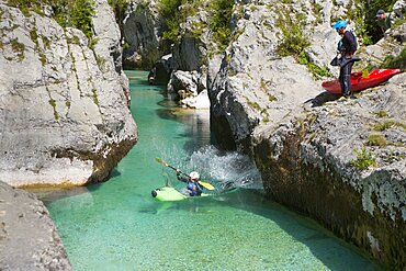 A man in a kayak is jumping into the water, while another man is watching. The emerald Soca near Bovec in Slovenia, originating in the Triglav mountains, is famous for all kinds of white water activities.