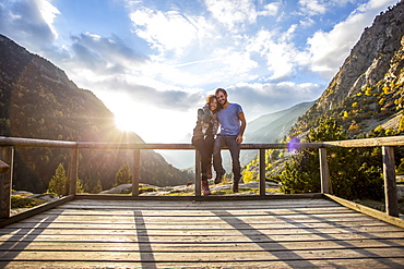 Portrait of young couple embracing on wooden platform in Aiguestortes i Estany de Sant Maurici National Park at sunset, Aiguestortes, Lleida, Spain