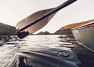 Mountains in Maine's Acadia National Park are framed by a paddle, water droplet and a canoe while they are paddling on Jordan Pond.