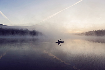 Young woman enjoys early morning paddle in kayak through mist on Daicey Pond in Maine's Baxter State Park, USA