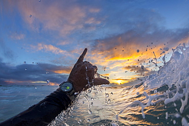 Person throwing shaka sign in surf at dawn