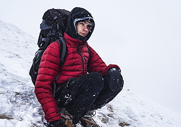 Teenage backpacker crouching while resting while trekking in winter in Tatra Mountains, Malopolskie Province, Poland