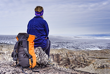 Rear view of woman sitting with backpack and looking at view of glacier, Narsaq, Greenland