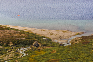 Distant view of person paragliding after base jumping from the top of Ulamertorsuaq, 1000m high granite tower in the Tasermiut Fjord, South Greenland