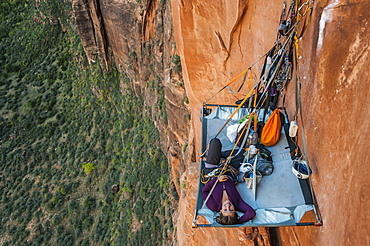 View from above of single young woman lying on portaledge while rock climbing Moonlight Buttress, Zion National Park, Utah, USA