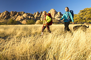 Mother and daughter hiking through dry grass below Sheepshead in Cochise Stronghold, Tombstone, Arizona, USA