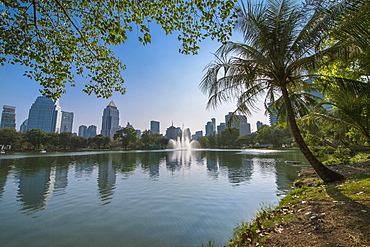 View of fountain in lake at Lumphini Park under clear sky and skyline of city of Bangkok, Thailand