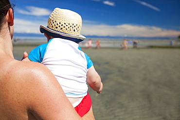 Over the shoulder view of mother carrying baby boy on beach