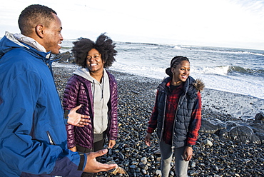 Three smiling African American people standing on gravel beach and talking