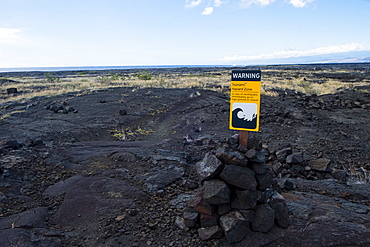 Tsunami Hazard Zone warning sign in bright yellow stands out from the landscape along the famed Puna Coast Trail to Halape Beach. The trail is 11.3 miles of rugged hiking for backpackers with no shade or water in the extreme terrain of Hawaii Volcanoes National Park, Hawaii, USA