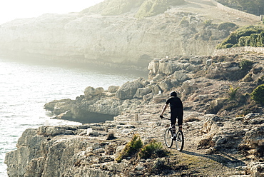 Rear view shot of adventurous mountain biker riding on coastal cliffs