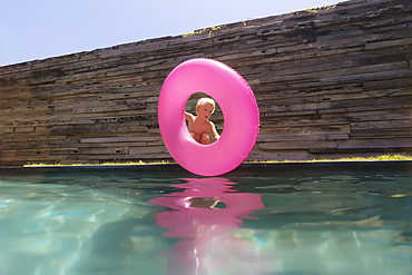 Single blonde boy with pink inflatable ring near swimming pool