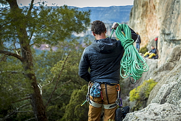 Rear view shot of male rock climber carrying rope to cliff, Siurana, Catalonia, Spain