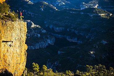 Distant view of single adventurous rock climber standing on edge of cliff after successful climb, Margalef, Catalonia, Spain