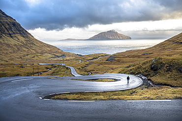 Distant view of man walking on winding road on seashore, Faroe Islands, Denmark