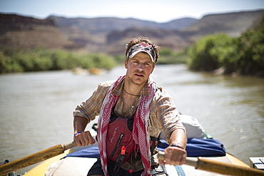 Raft guide man rowing and looking at camera during rafting trip, Desolation/Gray Canyon section, Utah, USA