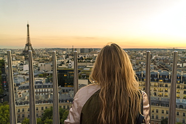 Rear view shot of single woman looking at view of Paris at sunset from Triumphal Arch, France