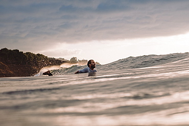 Professional surfer Jonathan Gonzalez paddling back to peak as sun sets, Tenerife, Canary Islands, Spain