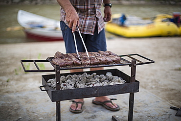 Raft guide with cooking steaks on grill in outdoor kitchen during Green River rafting trip, Desolation/Gray Canyon, Utah, USA