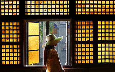 Woman in white lace dress and hat in hallway in front of capiz (shell) window in San Agustin Church, Manila, Philippines