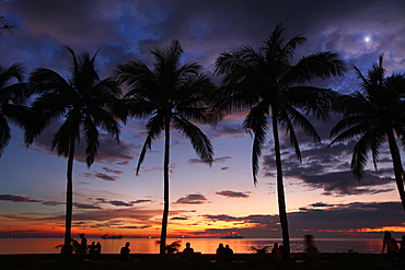 Silhouettes of people and palm trees against sky and sea at sunset, Manila, Philippines