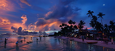 View of beach with silhouettes of tourists and palm trees at sunset, Boracay, Aklan, Philippines