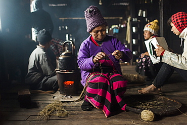 Elderly woman wearing knit hat knitting indoors in small rural house, Myanmar, Shan, Myanmar