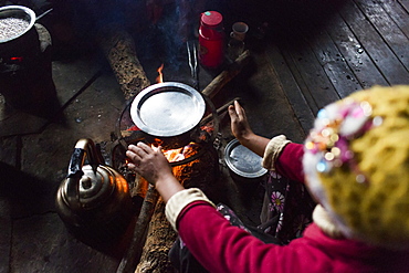 Arms of woman sitting in front of indoor campfire and warming hands, Myanmar, Shan, Myanmar