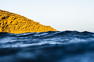 View of yellow rocky cliff sticking out of blurred dark blue ocean at daytime, Montana Pelada, Tenerife, Spain