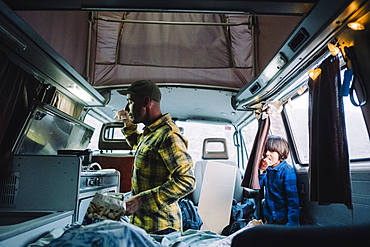 Man cooks in camper van as his son looks from the door, Tenerife, Canary Islands, Spain