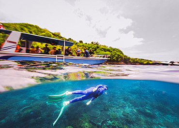 Freediver hanging underwater under tour boat full of tourists, Nusapenida, Bali, Indonesia