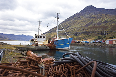 Rusty chains in front of old abandoned fishing boat moored in harbor of small coastal town, Seydisfjordur, Iceland