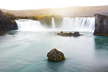 Long exposure of scenic Godafoss waterfall lit by golden sunlight at dusk, Iceland