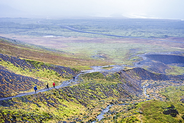 Group of four hikers walking in rain across Raudfeldsgja Ravine in Snaefellsnes peninsula, Iceland