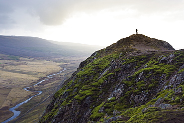 Silhouette of female hiker standing on top of mossy mountain overlooking river, Geysir, Iceland