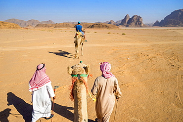 First person perspective riding camel through desert of Wadi Rum, protected desert wilderness in southern Jordan, with sandstone mountains and man riding camel in distance, Wadi Rum Village, Â AqabaÂ Governorate, Jordan