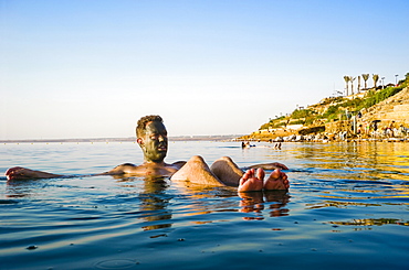 Man with mud on face floating in Dead Sea, Madaba Governorate, Jordan