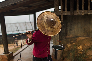 Young woman wearing hat carrying buckets with water on carrying pole, Myanmar, Shan, Myanmar