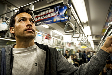 Man standing in subway car full of people, Tokyo, Japan