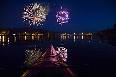 Fireworks go off in background with silhouetted view of paddle board on Long Lake 4th of July, New York, USA