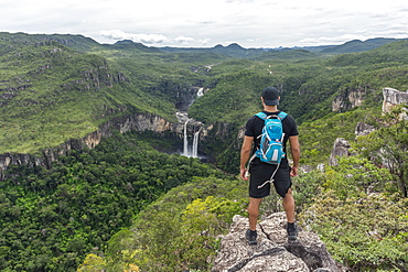 Young adult standing on rocky edge with beautiful natural cerrado landscape on the background, Mirante da Janela hike, Chapada dos Veadeiros, Goias, central Brazil