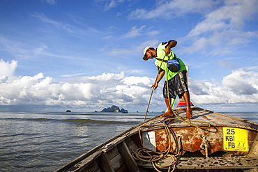 A boat captain raises the anchor on a boat along that coast of Krabi, Thailand before a ride to Railay Beach, a popular tourist destination.